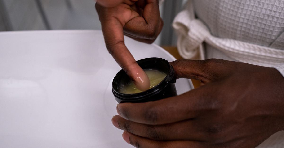 Hands applying a thin layer of ointment to a healing tattoo on an arm